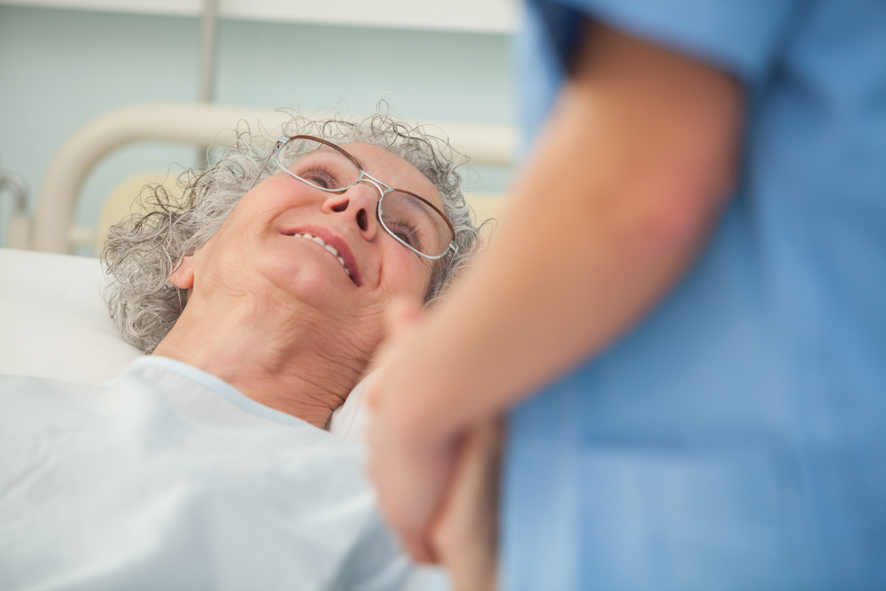 Elderly female patient looking up at nurse from hospital bed